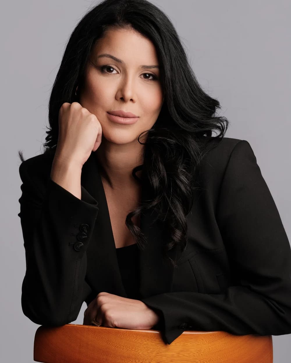 Tatiane Martins sentada, com blazer preto, em retrato profissional
